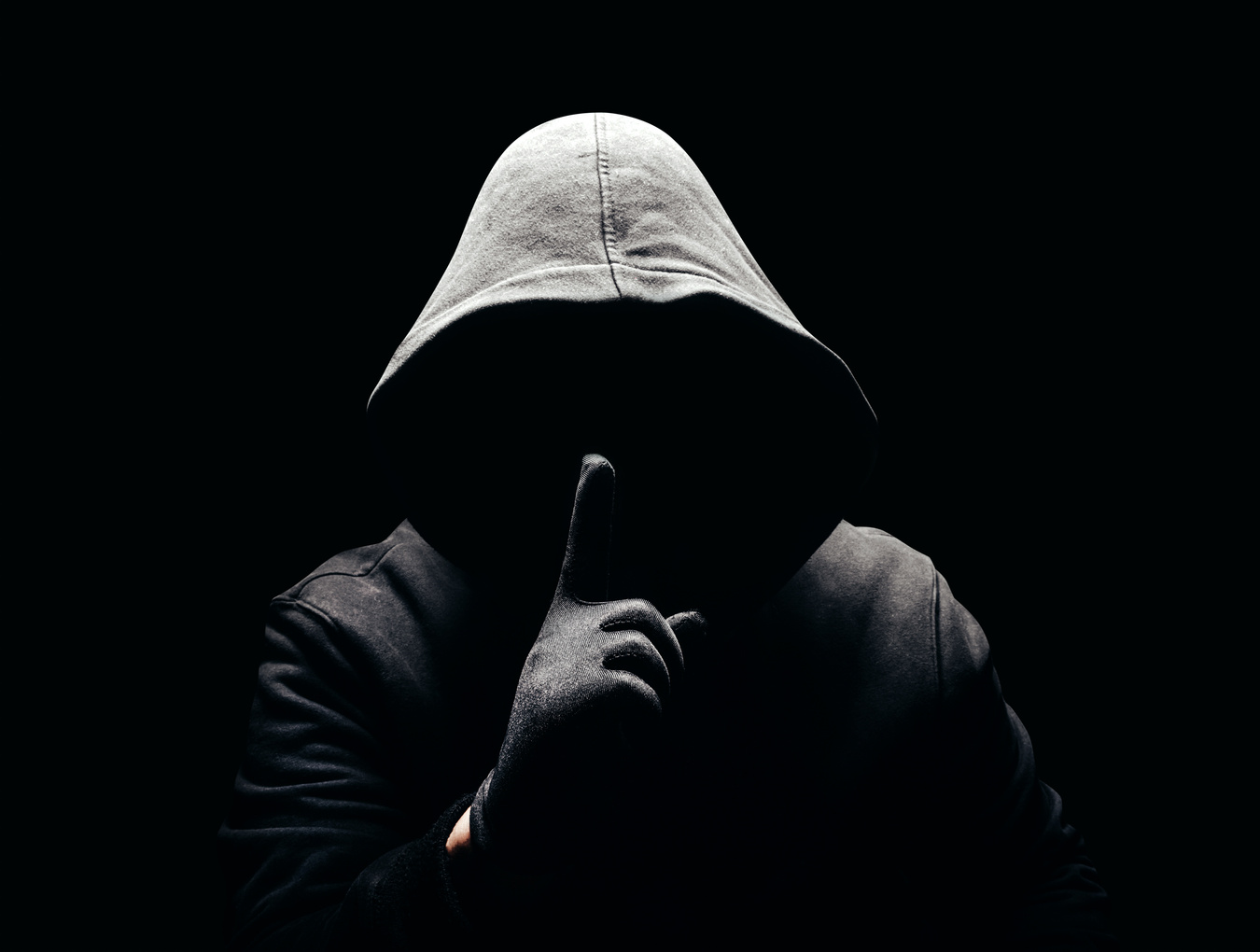 Horror man in hoodie showing silence hand sign in dark.